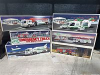 Six original vintage Hess trucks and emergency vehicles in their boxes, displayed on surface.