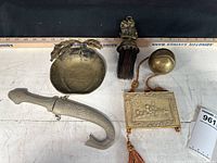 Five assorted brass decor items on white surface with ruler for scale, showing size and detail.