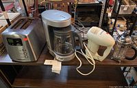 Photo showing the full set of four appliances on a wooden shelf: Cuisinart toaster, coffeemaker, handheld mixer and a French press.