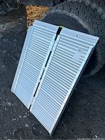 Folding aluminum ramp folded in half, showing ridged aluminum surface and hinges in the middle.