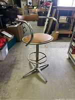Side and angled view of metal mid century stool showing tubular curved backrest and round padded vinyl seat with adjustable height base.