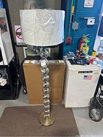 Full view of the floor lamp showing the white wrapped shade, stacked reflective glass ball base, and gold metal base.