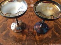 Two silver-tone champagne goblets with slightly tarnished surfaces on a wooden table.