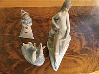 Photo of three porcelain figurines on wooden table: 10-inch girl figurine, 5-inch clown, 4-inch ducks group