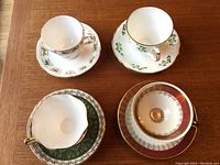 Top-down view showing four assorted fine bone china tea cups and their matching saucers, each with different decorative floral and gold trim designs.