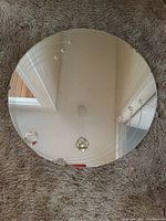 Photo of the round antique mirror approximately 24 inches in diameter, showing surface cracks and chips along the edge with visible scratches.