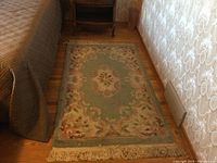 Rectangular Aubusson wool rug placed on wooden floor near bed, showing floral pattern and fringe edges.