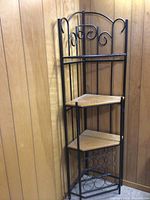 Tall corner baker's shelf with black metal frame, three wood shelves, and bottom metal wine rack