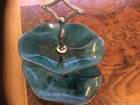 Front angled view of two-tier Blue Mountain ceramic candy tray in green glaze, approximately 12 inches high with gold-toned metal handle.