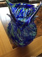 Photo of a 10-inch blue glass vase shaped like an owl with swirling blue, green, and amber tones, showing detailed owl face and form.
