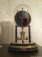 Full view of the Bulova mantel clock showing the glass dome cover, black dial with floral design, gold numerals, and pendulum.