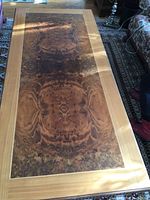 Top-down view of rectangular table top showing burl wood veneer pattern and light wood border