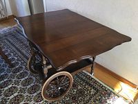 Side view of the solid walnut coffee and tea trolley with the leafs open to show the expanded top surface and two large wheels.