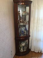 Corner curio cabinet assembled against wall, showing walnut finish, curved glass doors, mirrored back and interior light