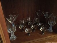 Photo showing 6 crystal shot glasses, 4 cocktail glasses, and 2 beer glasses arranged on shelf.