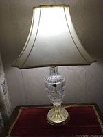 24% lead crystal table lamp with white fabric lampshade, turned on and photographed from the front.
