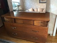 Walnut veneer low boy dresser with multiple storage drawers and an adjustable mirror attached to the back. The dresser is polished with brown wood grain finish and has two different styles of silver-tone handles on drawers.