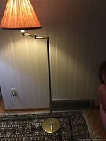 Floor lamp with brass finish and beige fabric shade, lamp is lit showing warm light.