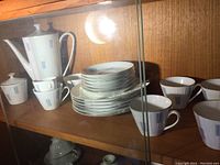 Photo showing a full set of vintage German coffee set including 6 coffee cups, 6 matching saucers, coffee pot, sugar bowl, and creamer pitcher inside a wooden cabinet.
