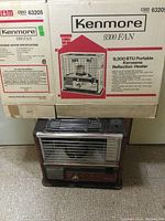 Kenmore 9300 BTU portable kerosene reflection heater with original packaging box shown behind the heater, placed on carpeted floor.
