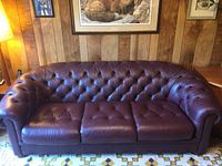 Full view of a burgundy leather sofa showing tufted design on backrest and cushions in a wood-paneled room.