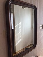 Rectangular wall mirror with thick walnut wood frame, showing reflection of room corner and window light.