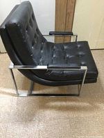 Side angle view showing black vinyl tufted padded seat and backrest with chrome metal frame and padded armrests.