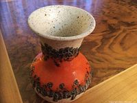 Stoneware vase with orange body and black textured details on a wood surface.