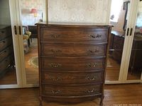 Front view of a walnut veneer tall boy dresser with 5 curved front drawers and ornate brass hardware. The dresser stands on four carved legs.