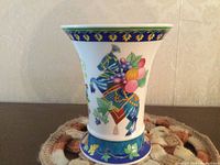 Front view of a 6-inch white porcelain vase with colorful hand painted decorations of a knight on a horse and fruit motifs on the body, blue and gold trim on rim and base.