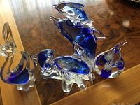 Photo showing five Venetian glass figurines: two large dolphins in blue and clear glass and three smaller fish figurines also in blue and clear glass with some metallic accents.