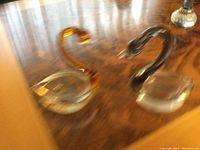 Photo of two Venetian glass swan figurines placed on a wooden surface, one amber colored and one smoke gray.
