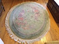 Oval Aubusson style wool rug with floral pattern and worn fringe laid on wooden floor