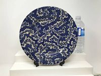 Front view of round ceramic charger plate with dark blue ornate floral and dragon pattern on white.
