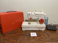 Singer Junior Miss child's sewing machine with orange carrying case and black foot pedal placed on wooden table, soda can for scale