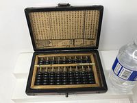 Open view of Chinese suan-pan abacus inside wooden case showing black beads and printed text inside lid
