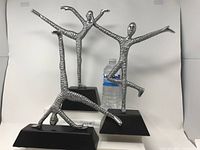Set of three silver metal art deco figurines in different dance poses on black stands with water bottle for scale