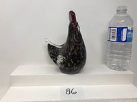 Side view of Murano glass rooster figurine next to water bottle for scale.
