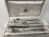 Five-piece cutlery set laid out in plum satin-lined case with label on lid.