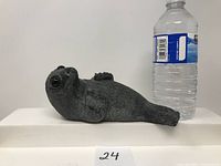 Side profile of the soapstone seal sculpture placed next to a standard water bottle for scale, showing detailed fur texture and body shape.