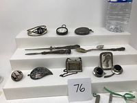Lot of 13 assorted sterling silver items displayed on white steps including bracelets, pocket watches, earrings, leaf-shaped brooch with abalone inlay, small spoons, and a pendant.