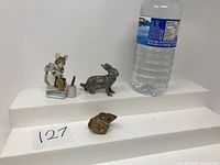 Three animal figurines displayed with water bottle for scale: Beatrix Potter mouse figurine, metal rabbit figurine, small brown pottery mouse figurine.