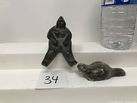 Front view of two sculptures, a seated Inuit figure and a seal, with bottle for scale.