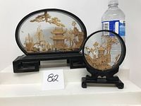 Two framed cork carvings on wooden stands against a white background with a water bottle for scale