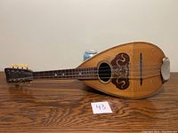 Front view of bowl-back mandolin showing spruce top, sound hole, decorative pickguard, floating bridge and metal tailpiece