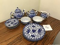 Top and front view of full set arranged on table showing teapot, sugar bowl, creamer, teacups with saucers, and luncheon plates decorated in blue and white Chinese design.