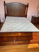 Full view of the wooden bed frame with high headboard and mattress on top, showing size and finish.