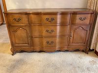 Front view of wooden cabinet showing three central drawers and two side doors with hardware and curved legs.