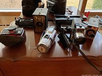 Photo showing various vintage cameras including Kodak Brownie Junior Six-16, Yashica, and camcorder on wooden table near window.