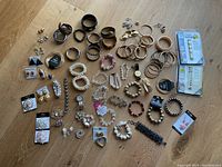 Wide shot of the assortment of costume jewelry on a wooden surface showing multiple bracelets, earrings, watches and other accessories.
